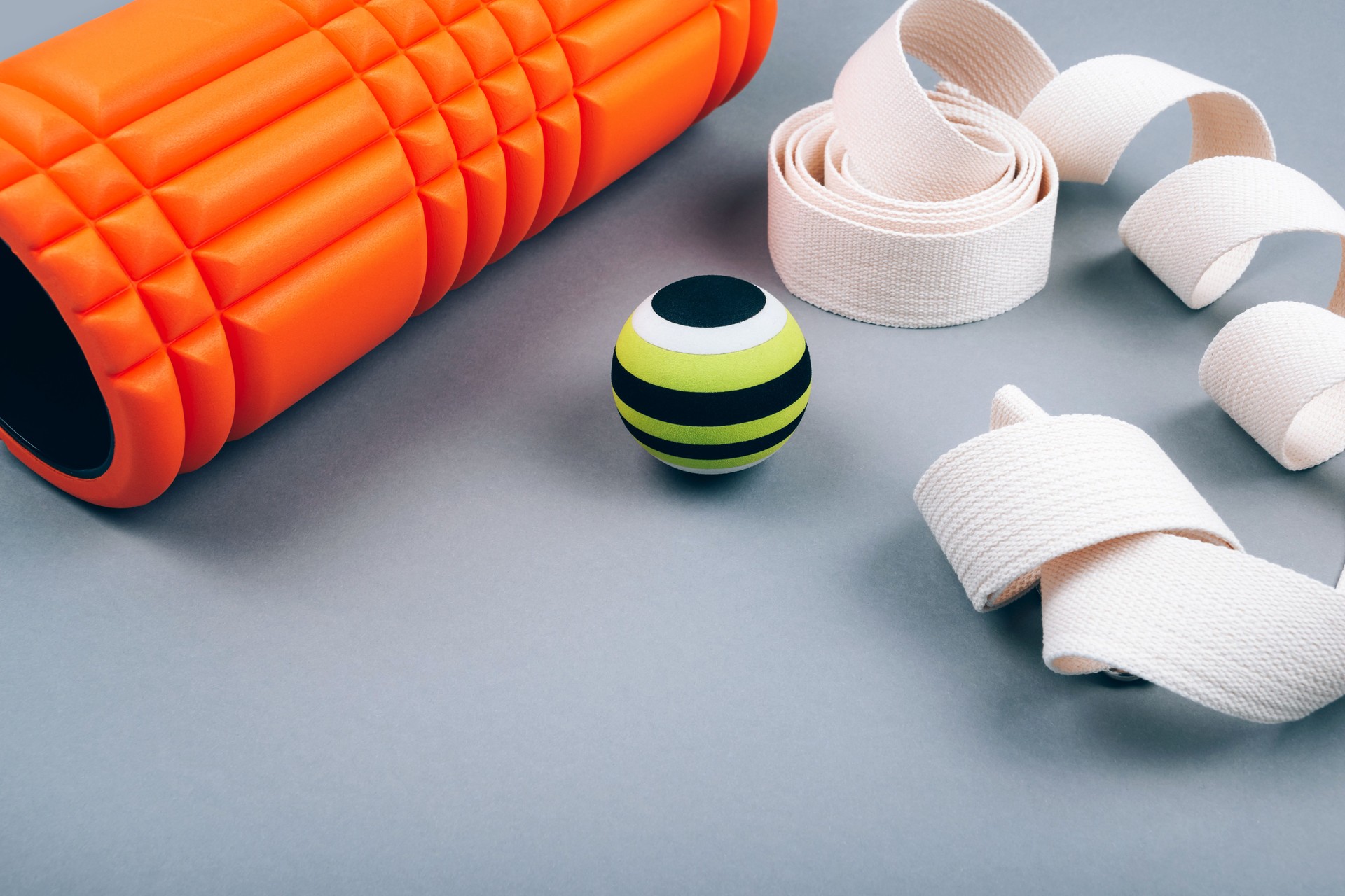 Set of green fascia release ball, orange bumpy foam massage roller for trigger points and belt over grey  background.